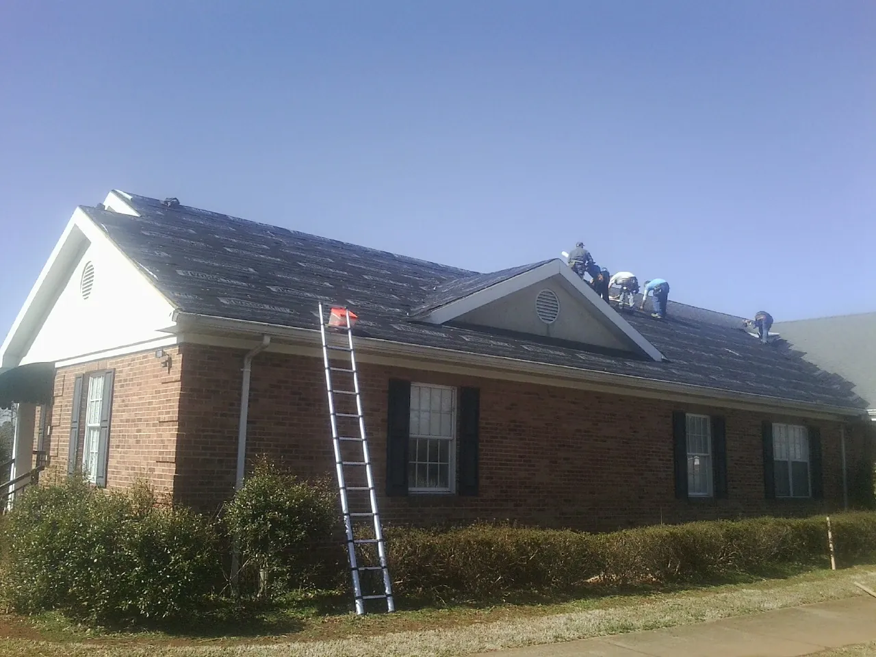 Crew tearing shingles off a brick ranch roof with a ladder set — Emergency Roof Repair work by our crew in Soddy Daisy