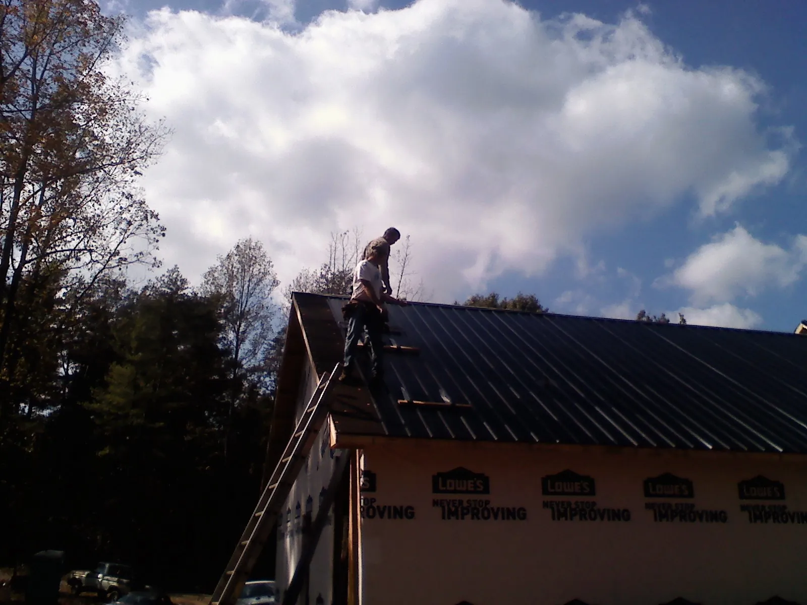 Roofer fastening dark metal panels high against a cloudy sky, from a Roof Inspection job in Soddy Daisy