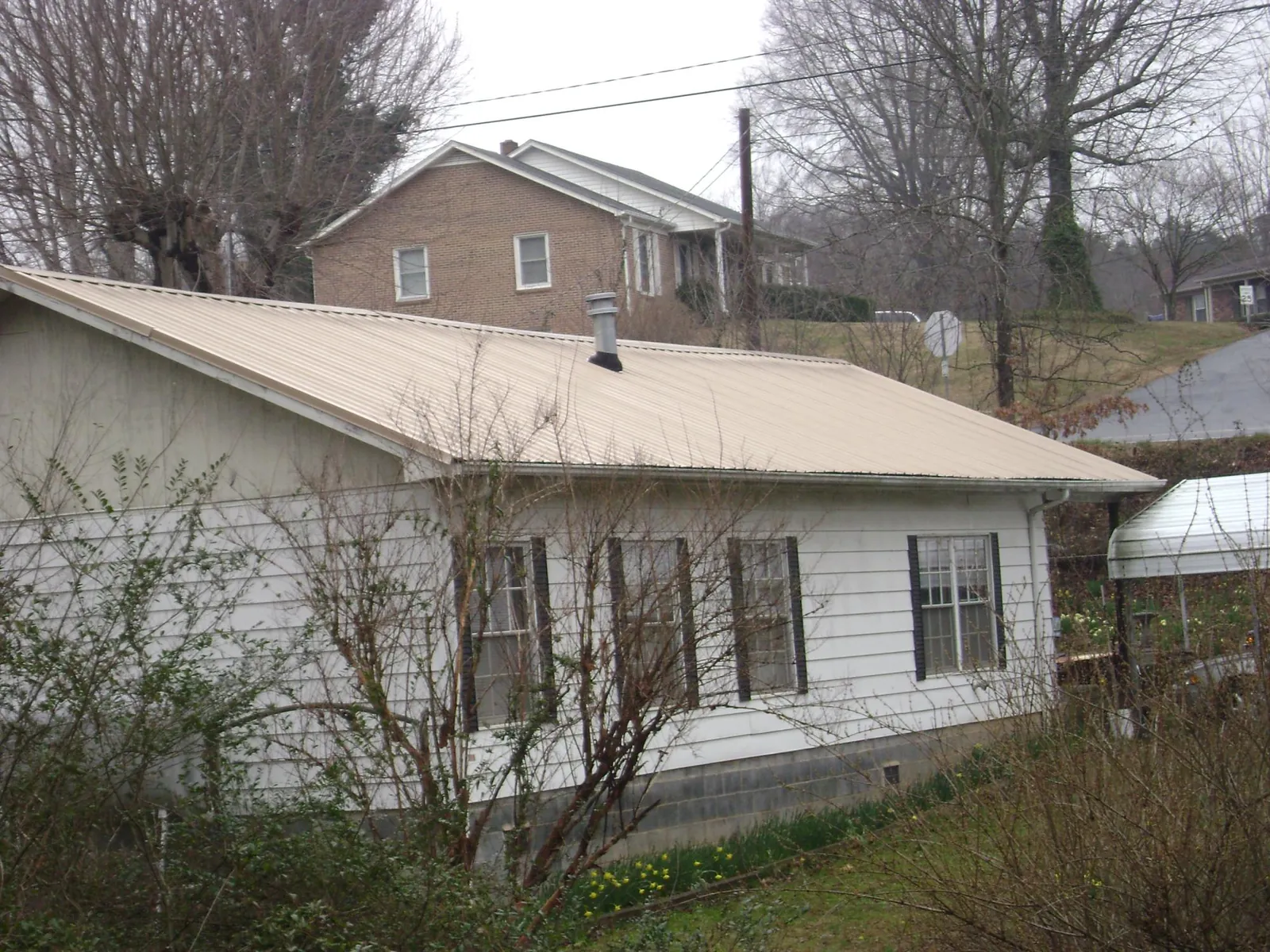 Tan metal roof on a white sided house set into a hillside — Commercial Roofing by Roofing Brothers in Soddy Daisy