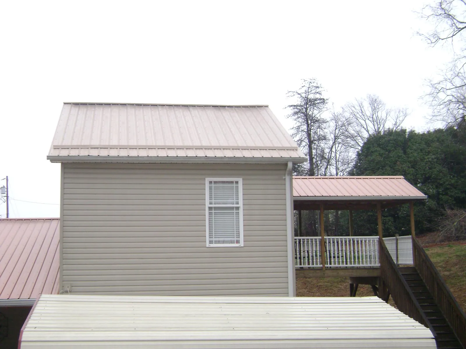 Tan metal roofs on a two story addition and attached porch, from a Roof Replacement job in Soddy Daisy